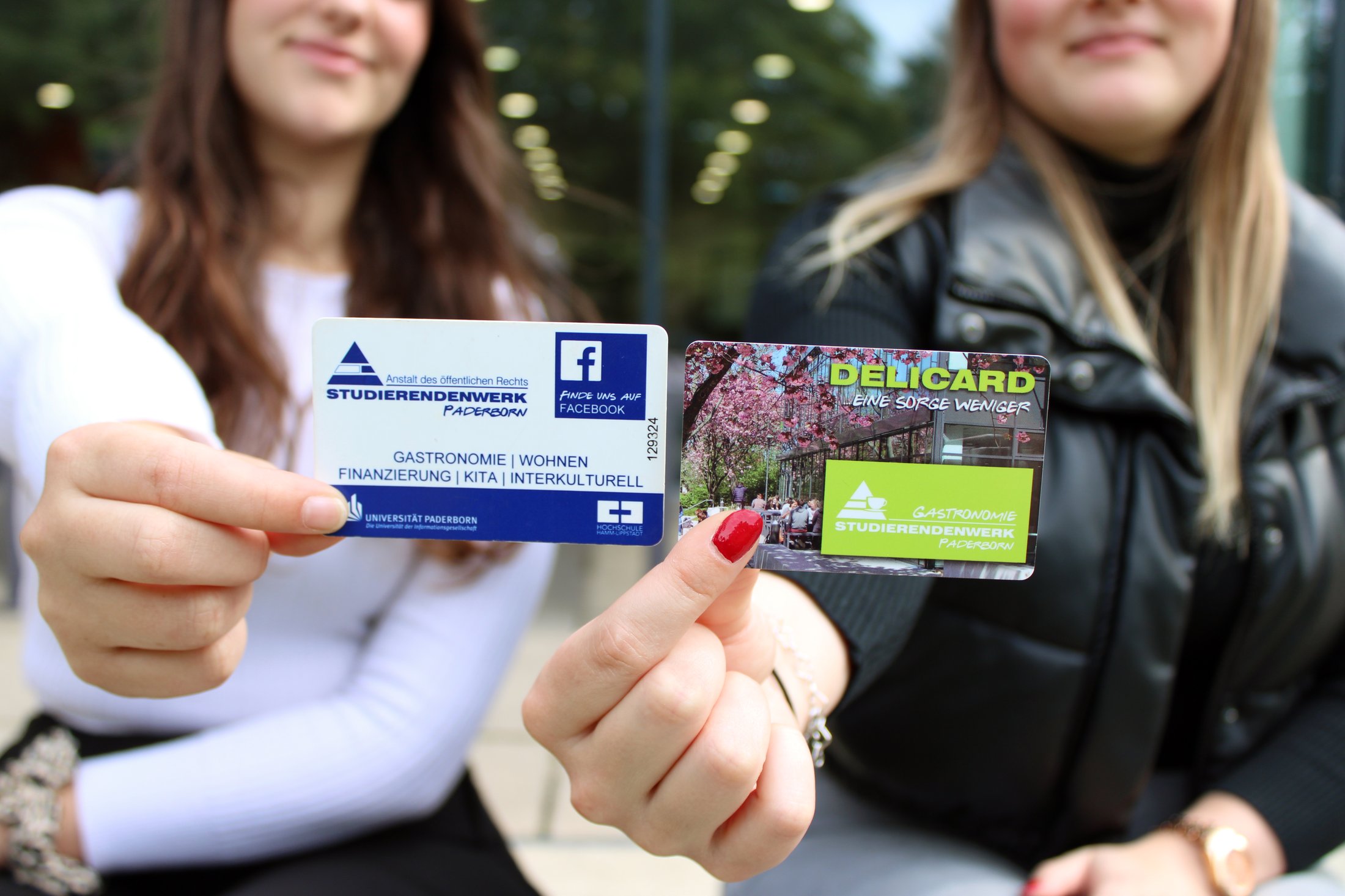 Zwei Karten werden in die Kamera gehalten: eine für das Studierendenwerk und eine DELICARD. Hintergrund unscharf.