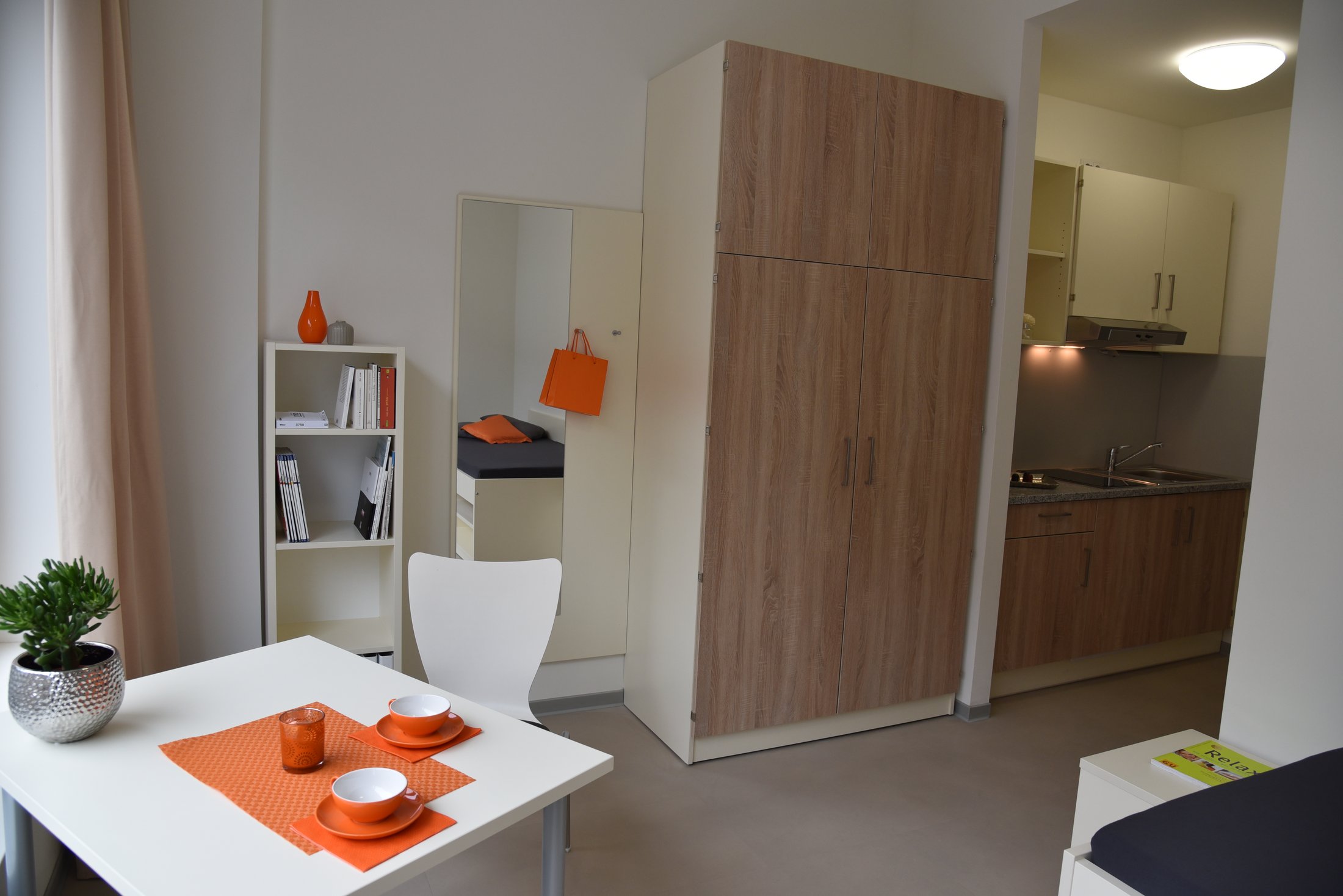 Studierendenwohnheim in Hamm: modernes Zimmer mit Küchenzeile, Tisch, Stühlen und freundlicher Dekoration.