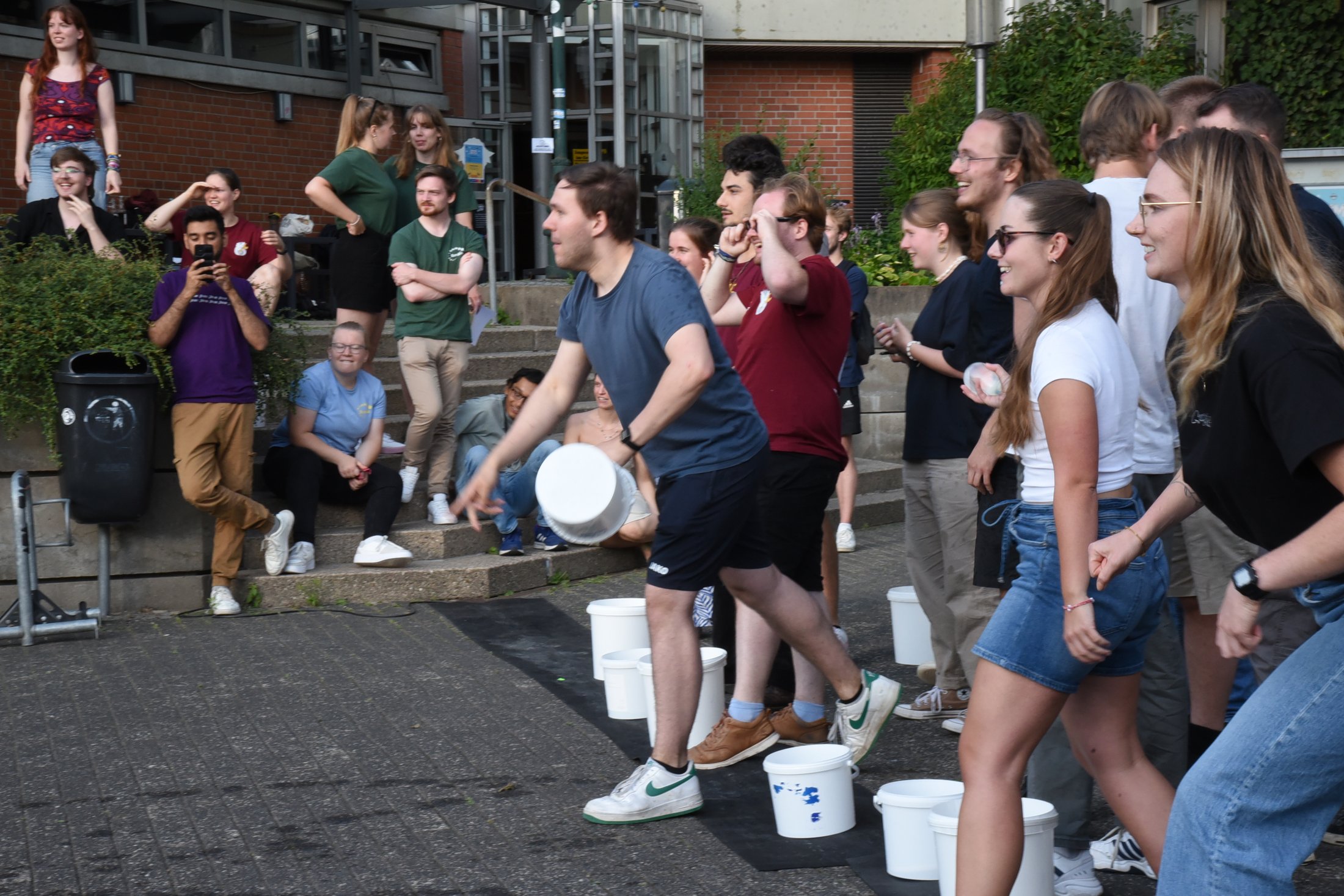 Gruppenspiel im Freien: Teilnehmende werfen mit Wasserbombe, um Ziele zu treffen. Zuschauer beobachten gespannt.