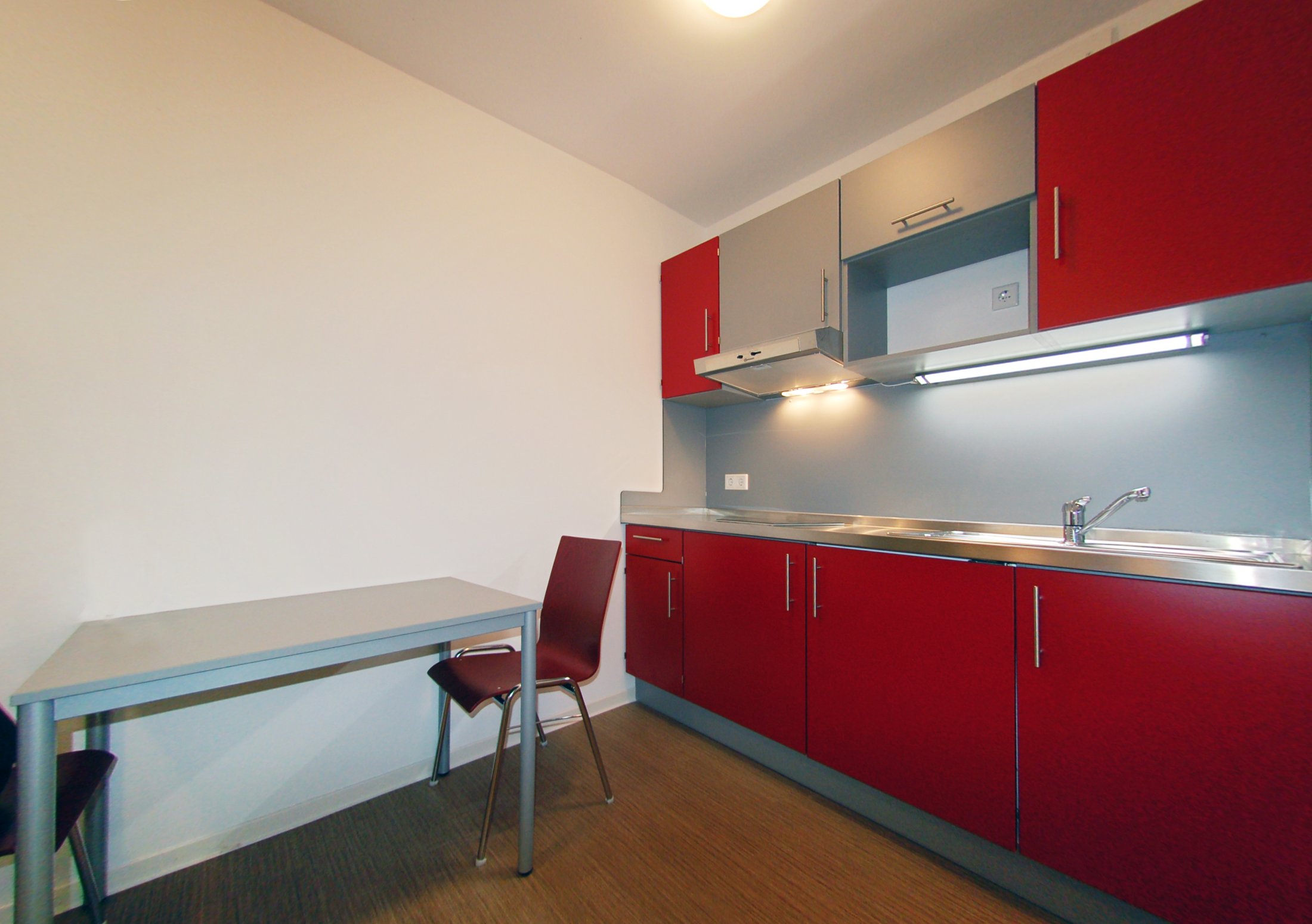 Küche in einem Studierendenwohnheim in Lippstadt mit roten Schränken, Tisch und zwei Stühlen.