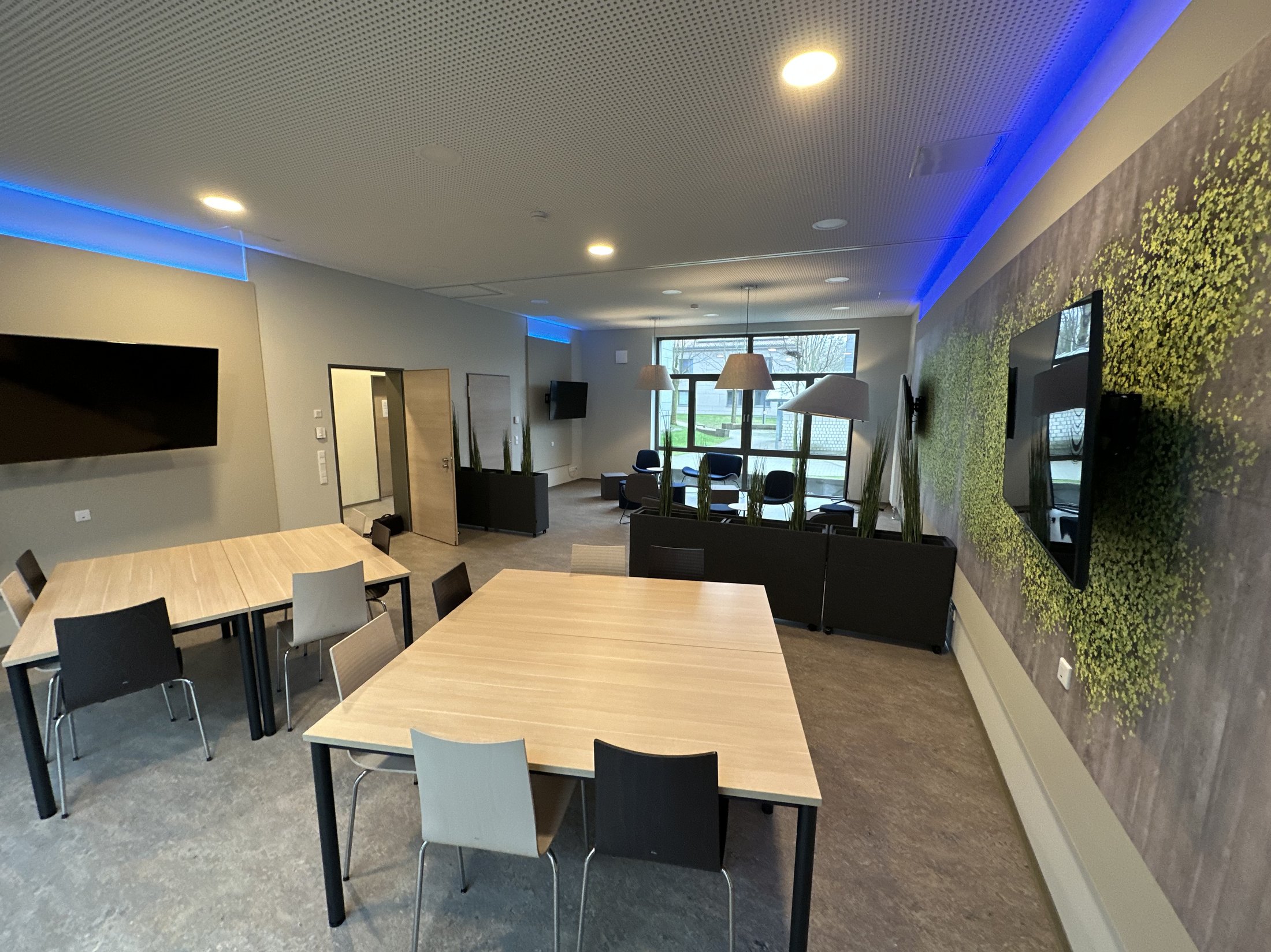 Moderne Lounge im Studierendenwohnheim Paderborn-Lernraum_Vogeliusweg mit Tischen, Stühlen und Pflanzen.
