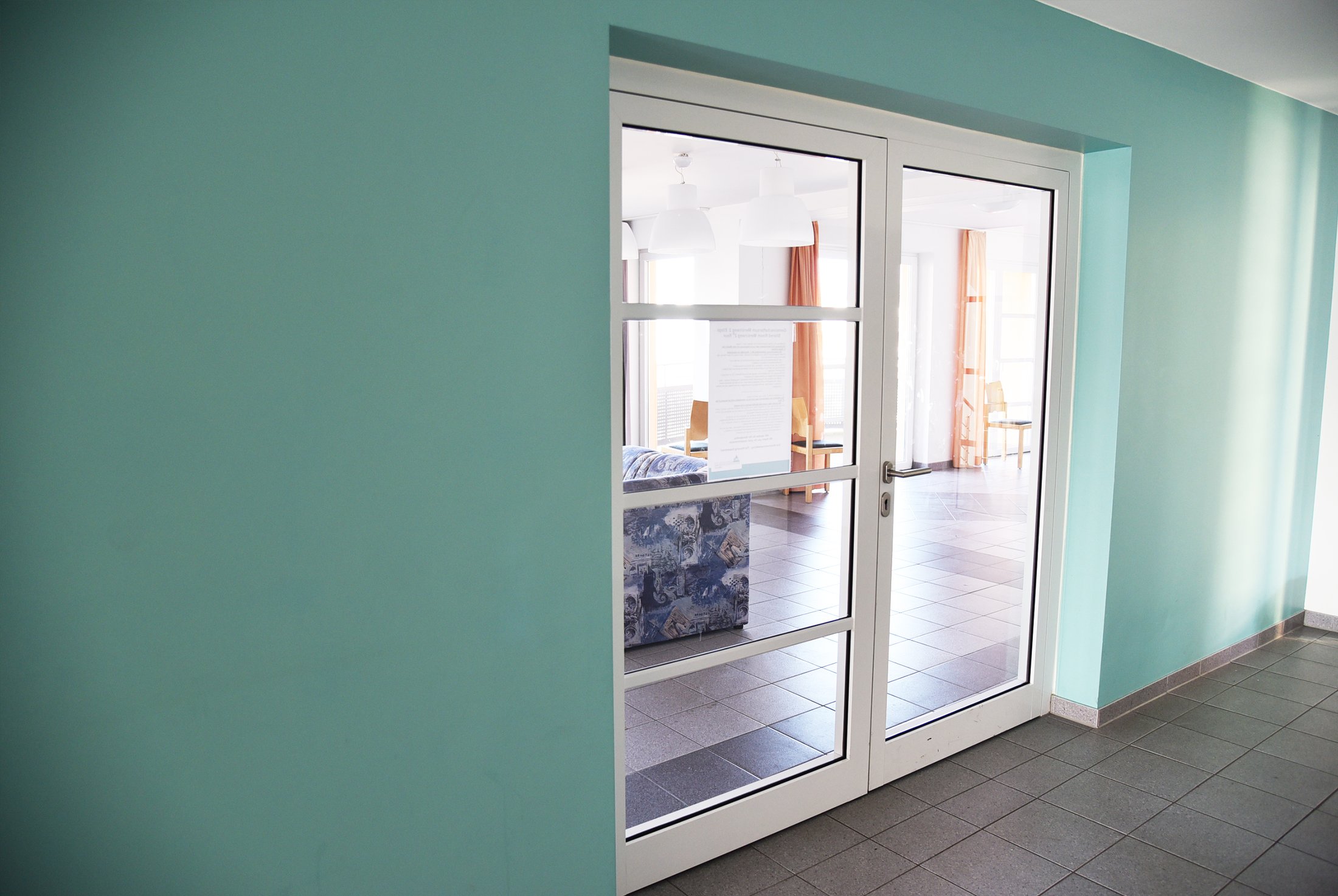 Durch eine Glastür sieht man einen hellen gemeinsamen Raum im Studierendenwohnheim Paderborn-Mersinweg_4.