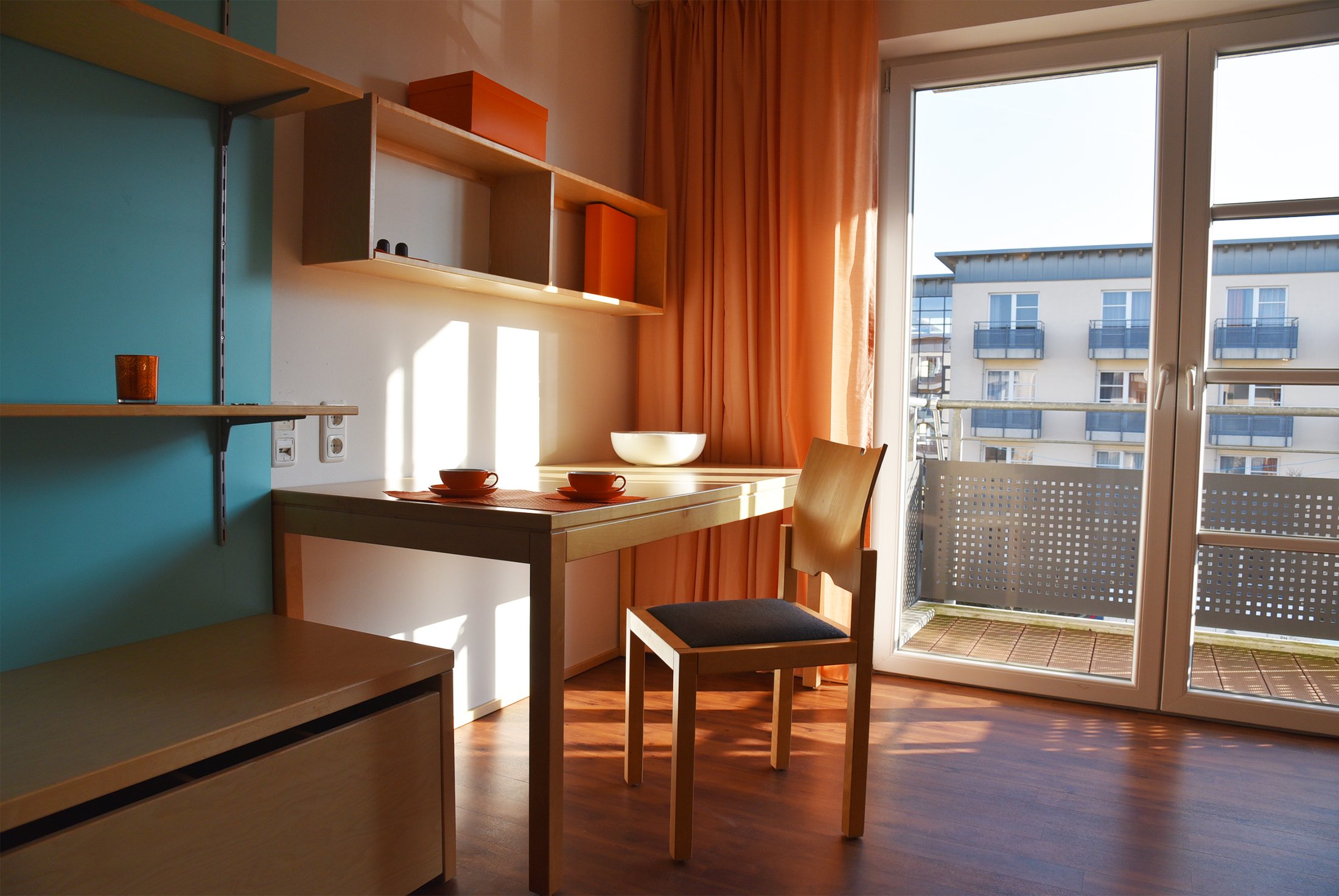Helles Zimmer im Studierendenwohnheim Paderborn-Mersinweg_4 mit Tisch, Stuhl und Blick auf den Balkon.