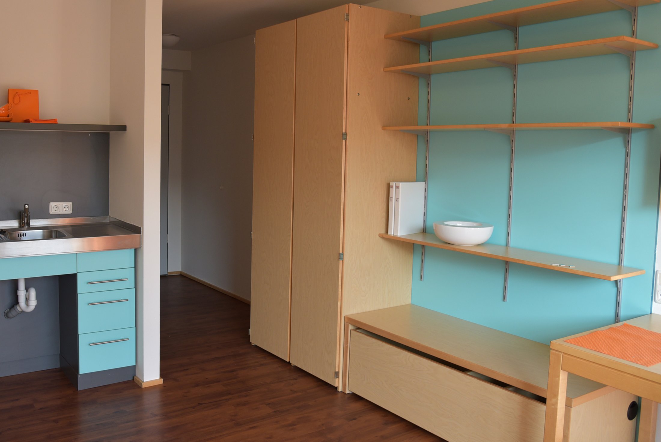 Studierendenwohnheim Paderborn-Mersinweg_4: Modernes Zimmer mit Küchenzeile, Regalen und warmen Holzton.