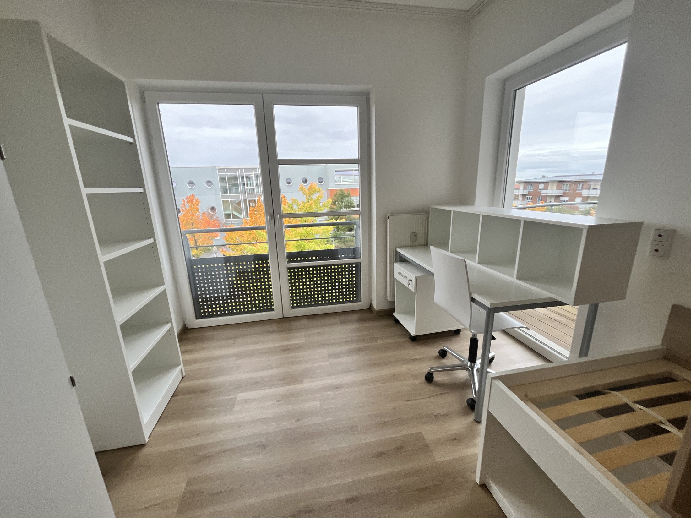 Helles Zimmer im Studierendenwohnheim Paderborn-Mersinweg_4 mit Schreibtisch und Blick auf Bäume.