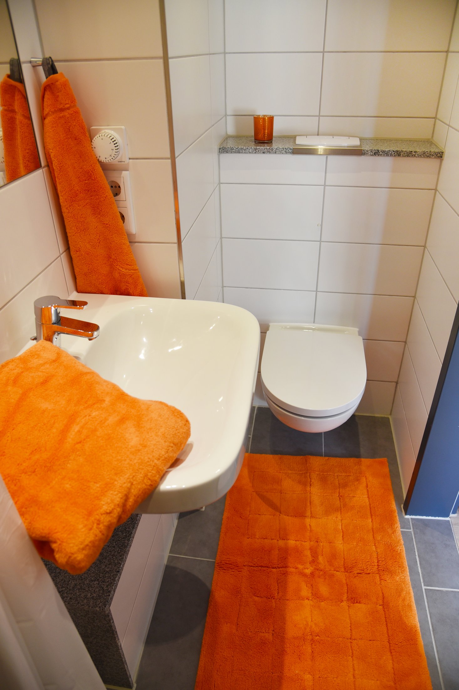 Badezimmer im Studierendenwohnheim Paderborn-Peter_Hille_Weg_11 mit hellen Fliesen und orangen Handtüchern.
