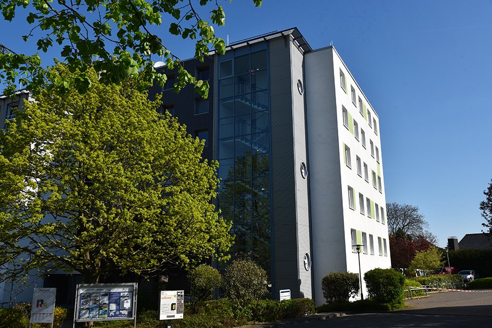 Studierendenwohnheim in Paderborn-Peter Hille Weg 13, modernes Gebäude umgeben von Bäumen und Grünflächen.