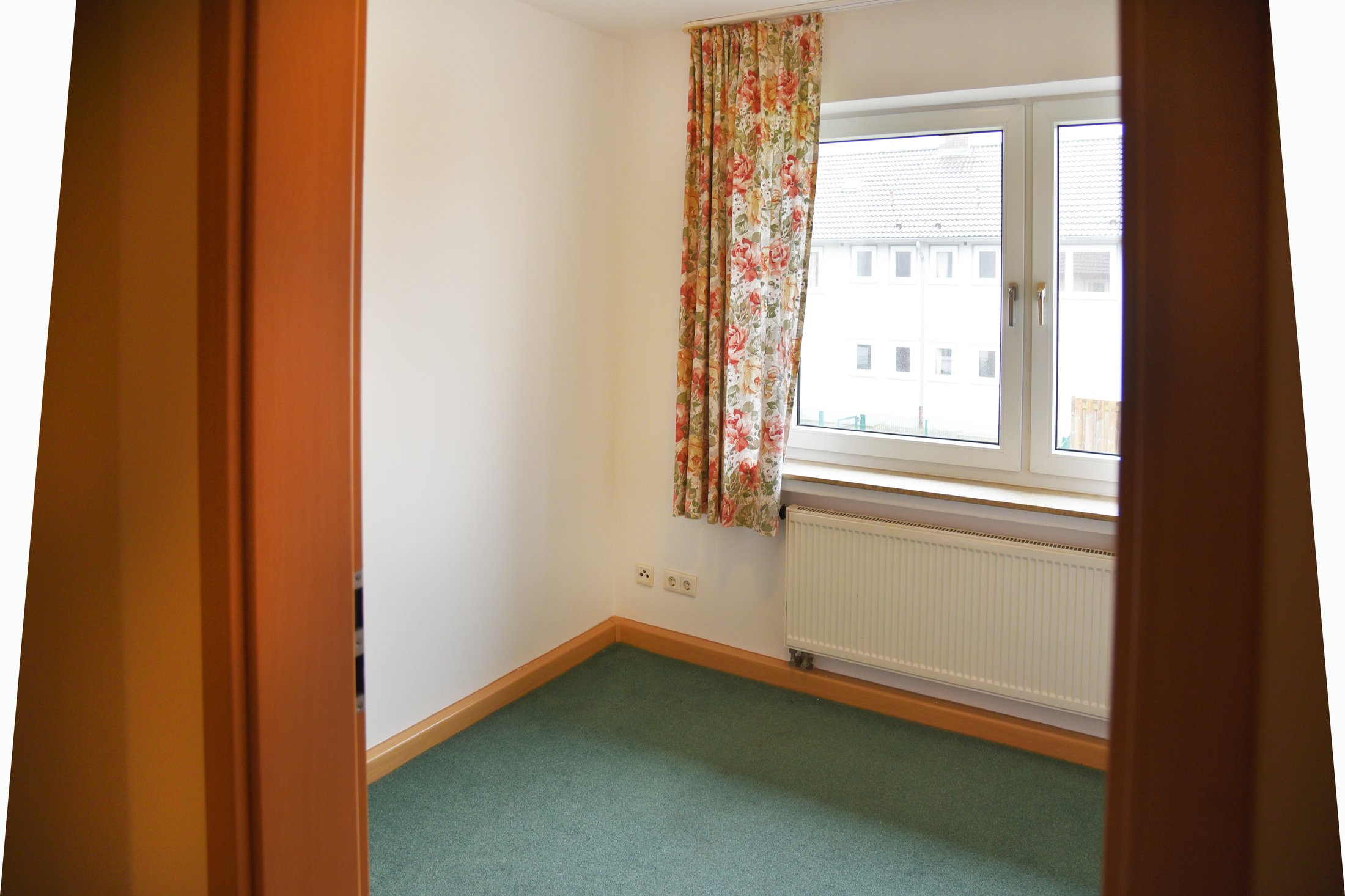 Ein helles Zimmer im Studierendenwohnheim Paderborn-Uhlandstraße mit Teppich und Fenster mit Vorhängen.